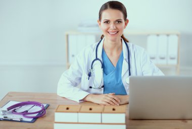 Güzel, genç, gülümseyen bayan doktor masada oturuyor ve yazıyor..