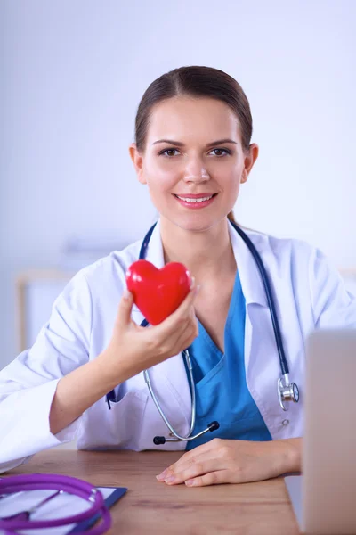 Young doctor with red heart symbol sitting at desk — Stock Photo, Image