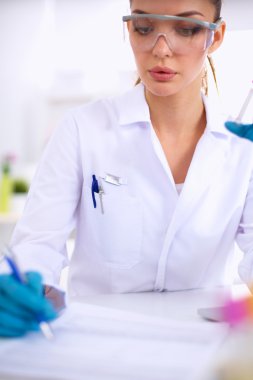 Kadın araştırmacı, beyaz arka planda izole edilmiş ilaç şişeleri ve mataralarla çevrili.