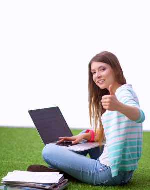 Yeşil çimenlerin üzerinde oturan ve ok gösterilen laptop ile genç kadın