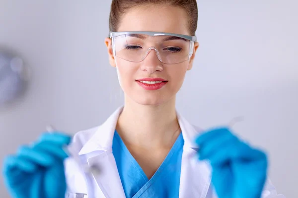 Dentista feminino atraente com ferramentas, de pé sobre fundo cinza — Fotografia de Stock