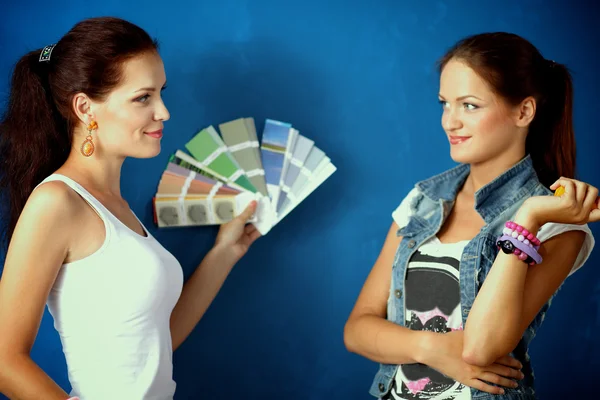Twee jonge mooie vrouwen houden kleurenpalet, permanent in de buurt van muur. — Stockfoto