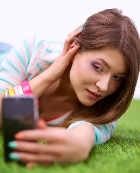 Krásná mladá žena, což selfie její telefonicky vleže v zelené trávě — Stock fotografie
