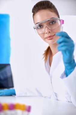 Kadın araştırmacı, beyaz arka planda izole edilmiş ilaç şişeleri ve mataralarla çevrili.