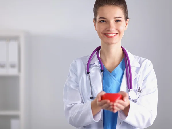 Mujer joven doctora sosteniendo un corazón rojo, parada en el hospital — Foto de Stock