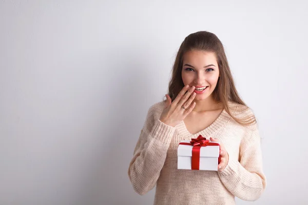 Молода жінка щаслива посмішка тримає подарункову коробку в руках, що стоїть над сірим тлом — стокове фото