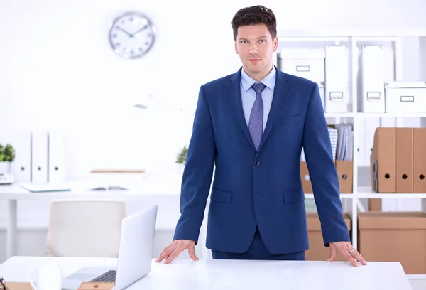 Hombre de negocios o gerente de pie contra su escritorio en la oficina —  Fotos de Stock