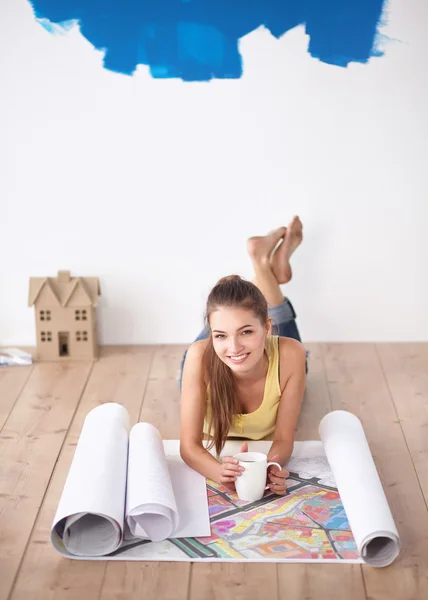 Ung kvinna liggande på golvet och tittar på blåkopia av nya hus — Stockfoto