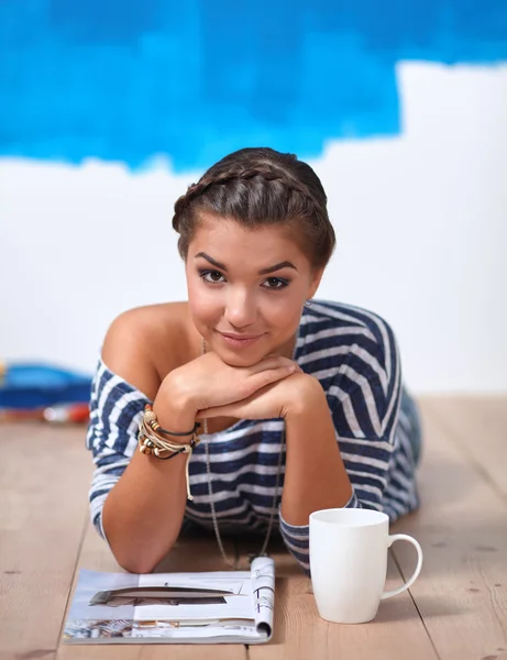 Portrait of female painter lying on floor near wall after paintingand holding a cup — Stock Photo, Image