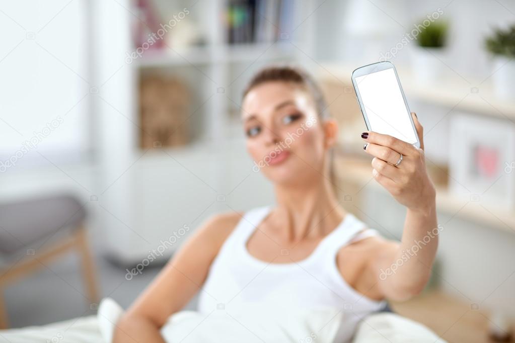 Happy brunette taking a photo of herself with her mobile phone in  bedroom