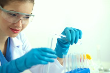 Kadın araştırmacı, beyaz arka planda izole edilmiş ilaç şişeleri ve mataralarla çevrili.