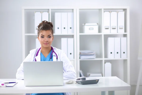 Female doctor sitting on the desk and working a laptop — Stock Photo, Image