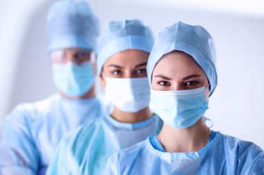 Cerrahlar, koruyucu üniformalar, kepler ve maskeler giyiyorlar.