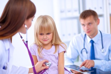 Kadın doktor ameliyatta steteskopla çocuğu muayene ediyor.