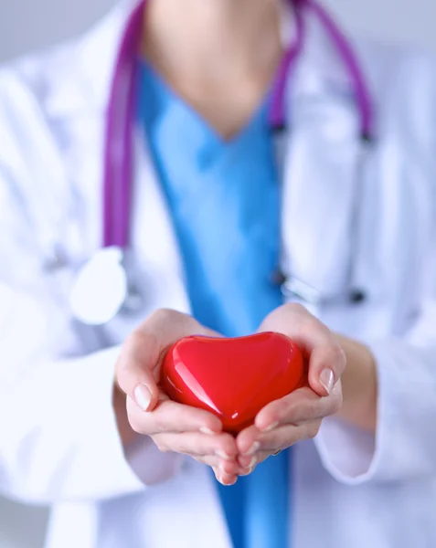 Mujer joven médico sosteniendo un corazón rojo, de pie sobre fondo gris — Foto de Stock