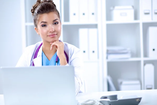Doctora sentada en el escritorio y trabajando en un portátil — Foto de Stock