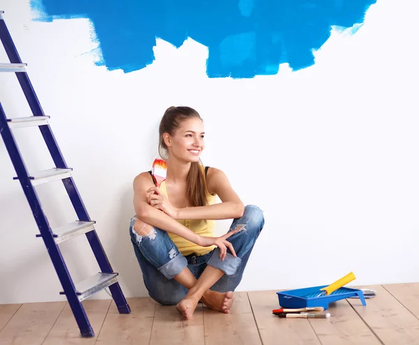 Portrét ženy malíře sedí na podlaze blízko zdi po malování. — Stock fotografie