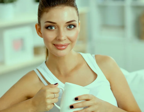 Young beautiful woman with a cup on sofa at home — Stock Photo, Image