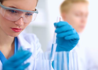 Kadın araştırmacı, beyaz arka planda izole edilmiş ilaç şişeleri ve mataralarla çevrili.