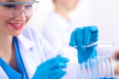 Kadın araştırmacı, beyaz arka planda izole edilmiş ilaç şişeleri ve mataralarla çevrili.