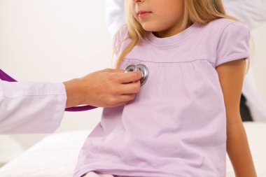 Kadın doktor ameliyatta steteskopla çocuğu muayene ediyor.