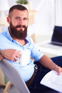 dizüstü bilgisayar ve bir çay bardağı evde oturan genç adam