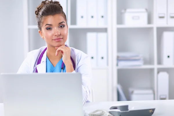 女性医師が机の上に座り、病院でノートパソコンを操作する — ストック写真