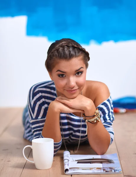 Retrato de pintora tendida en el suelo cerca de la pared después de pintar y sostener una taza —  Fotos de Stock