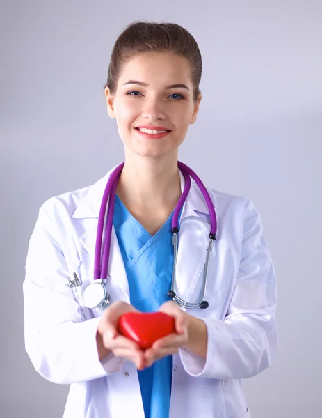 Kırmızı bir kalp taşıyan genç bir kadın doktor, gri arka planda duruyor. — Stok fotoğraf