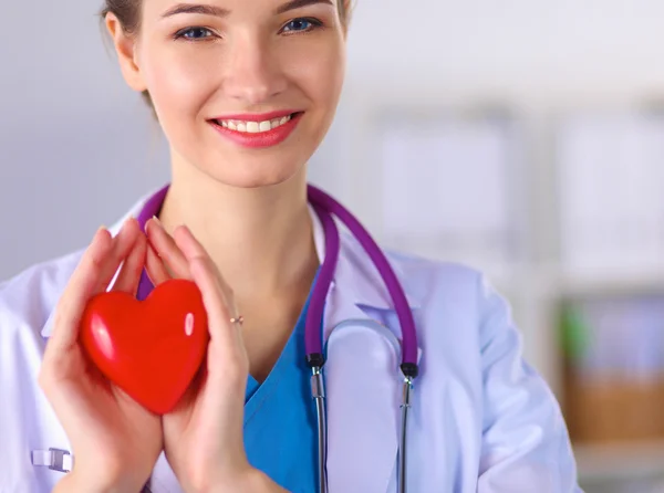 Νεαρή γυναίκα γιατρός κρατώντας μια κόκκινη καρδιά, στέκεται στο νοσοκομείο — Φωτογραφία Αρχείου