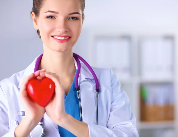 Genç bir kadın doktor elinde kırmızı bir kalp, hastanede duruyor.