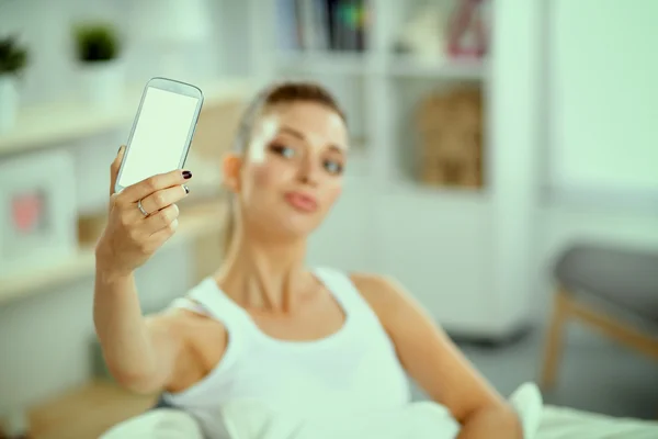 Gelukkig brunette nemen van een foto van haarzelf met haar mobiele telefoon in de slaapkamer — Stockfoto