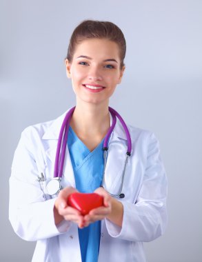 Genç bir kadın doktor elinde kırmızı bir kalp, hastanede duruyor.