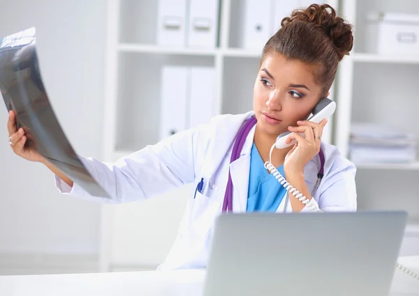 Женщина-врач ищет рентгеновские снимки и разговаривает по телефону в диагностическом центре, сидит за столом — стоковое фото