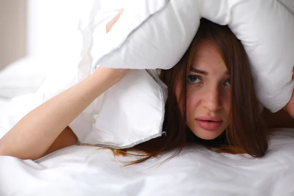 Mujer acostada en la cama y cerrando las orejas con almohada —  Fotos de Stock