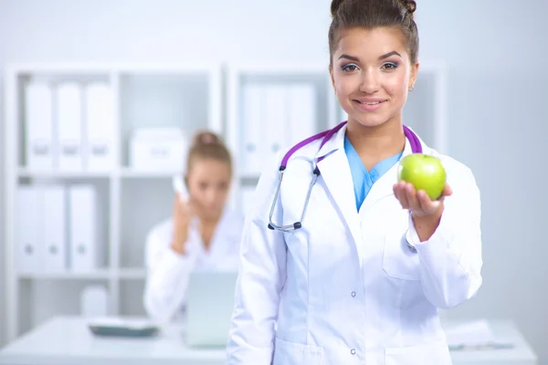 Женщина-врач держит за руку зеленое яблоко, сидит — стоковое фото