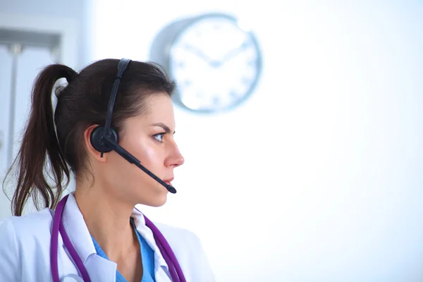 Portrait of young woman doctor in white coat at computer using phone — Stock Photo, Image