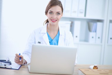 Kadın doktor masada oturuyor ve dizüstü bilgisayarla çalışıyor.