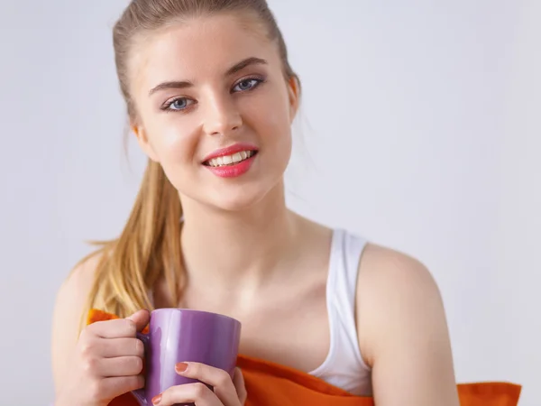 Mujer joven sentada con almohada y sosteniendo una taza de té —  Fotos de Stock