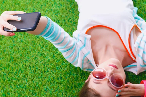 Mooie jonge vrouw selfie maken door haar telefoon liggend in groene gras — Stockfoto