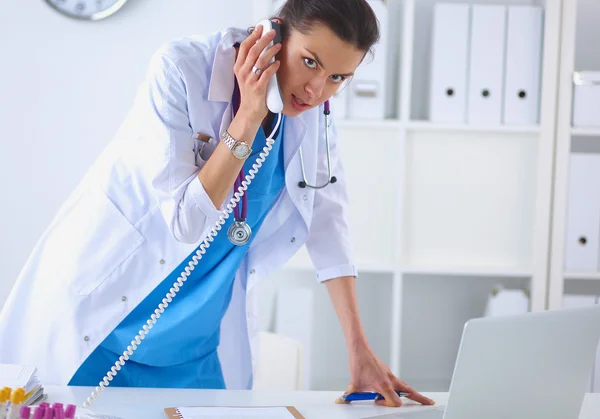 Junge Ärztin im weißen Kittel telefoniert am Computer — Stockfoto