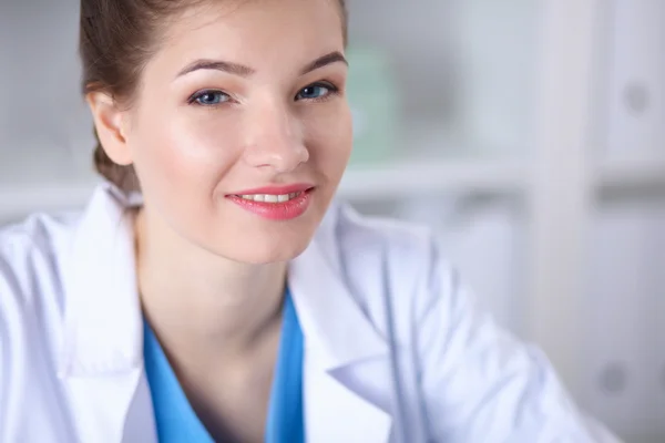 Hermosa joven sonriente doctora sentada en el escritorio . —  Fotos de Stock