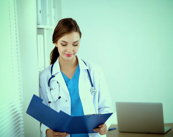 Kobieta lekarz stoi w pobliżu okna z skrzyżowanymi ramionami, odizolowany — Zdjęcie stockowe