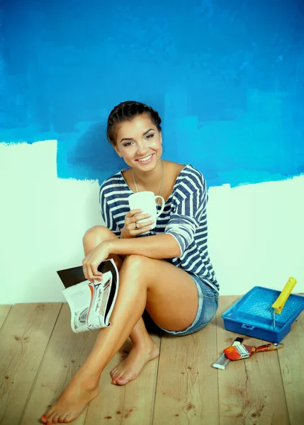 Portrait of female painter sitting on floor near wall after paintingand holding a cup — Stock Photo, Image