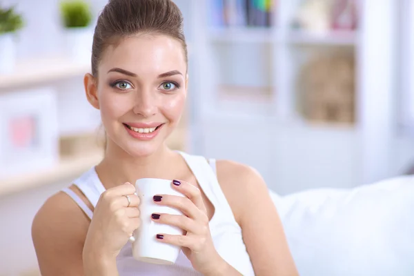 Portret van oung mooie vrouw met een kop op sofa thuis — Stockfoto