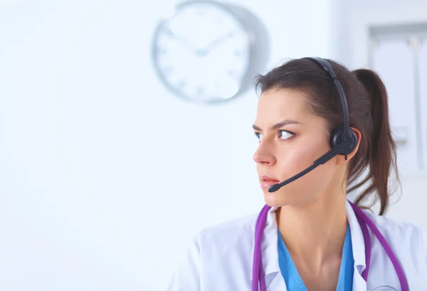 Médico usando fone de ouvido sentado atrás de uma mesa com laptop — Fotografia de Stock