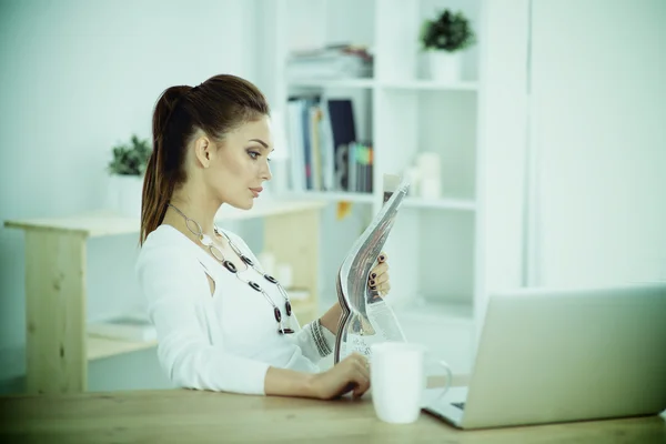 Cute businesswoman holding newspaper sitting at her desk in office — Stock Photo, Image