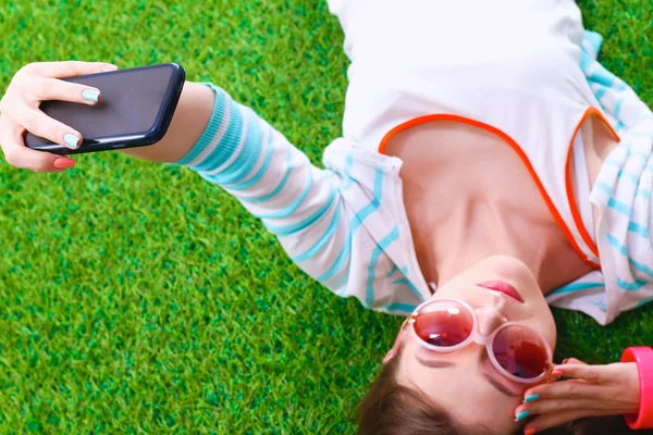 Bella giovane donna che fa selfie dal suo telefono mentre si trova in erba verde — Foto Stock