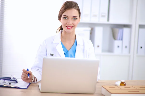 Doctora sentada en el escritorio y trabajando en un portátil — Foto de Stock