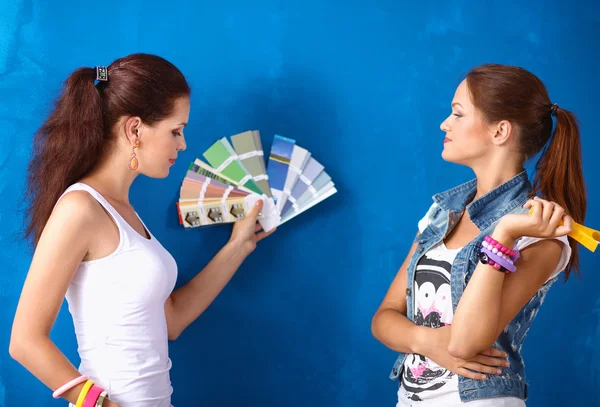 Duas mulheres bonitas jovens segurando paleta de cores, de pé perto da parede . — Fotografia de Stock